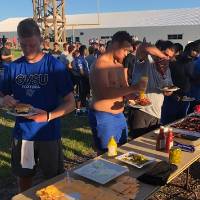 a line of football players waiting to be served food by the alumni